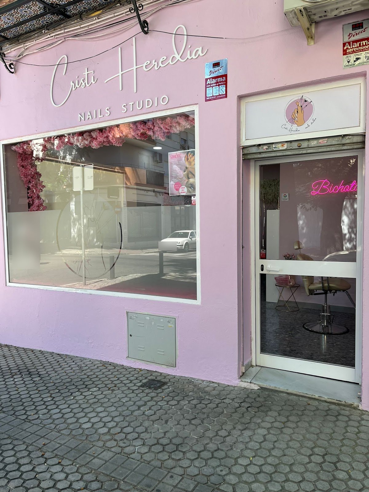 Fachada rosa de Cristi Heredia Nails Studio, con el nombre en letras blancas, un escaparate decorado con flores y la puerta abierta