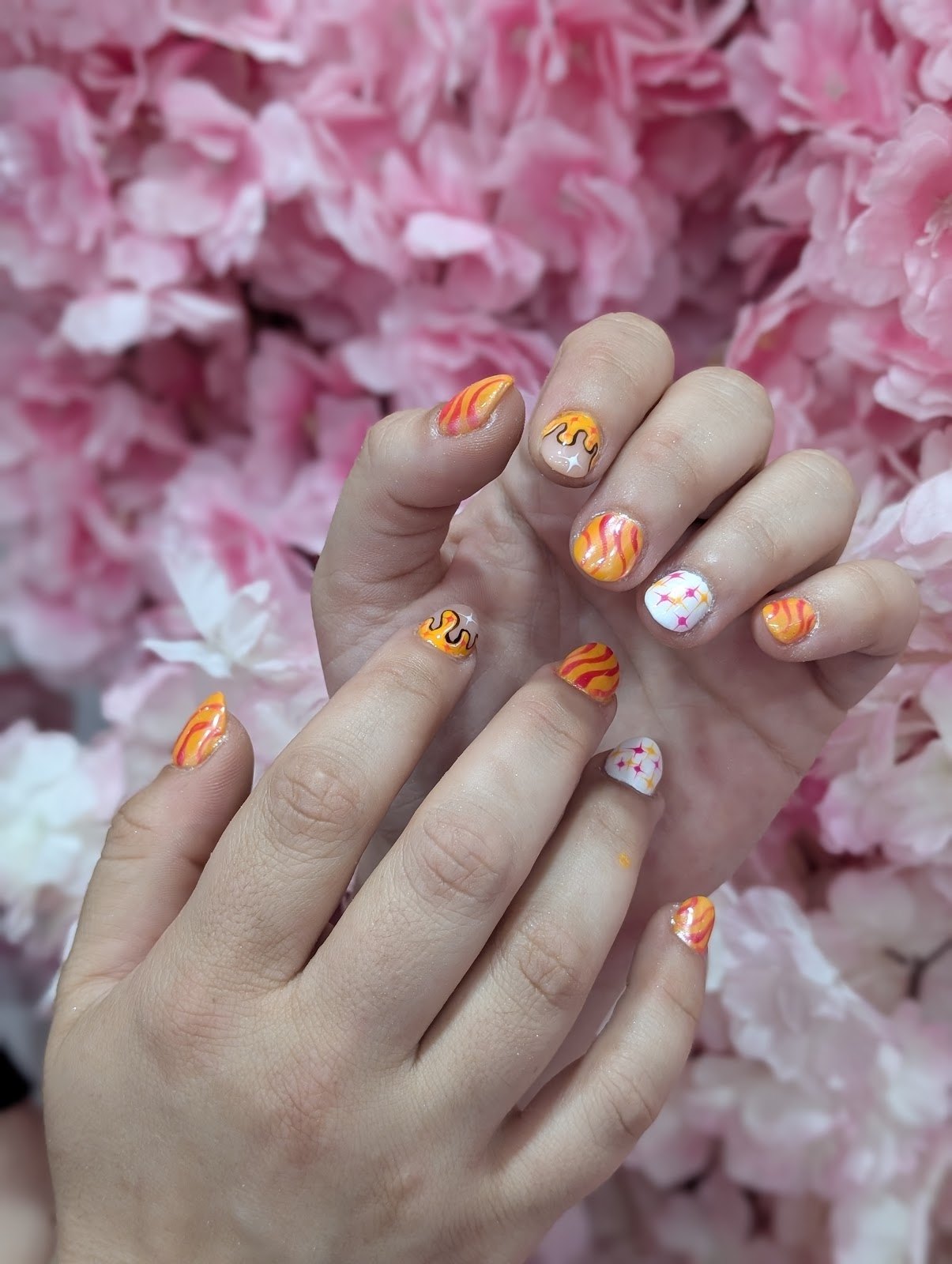 Uñas cortas con llamas naranjas y estrellas, sobre un fondo de flores rosas
