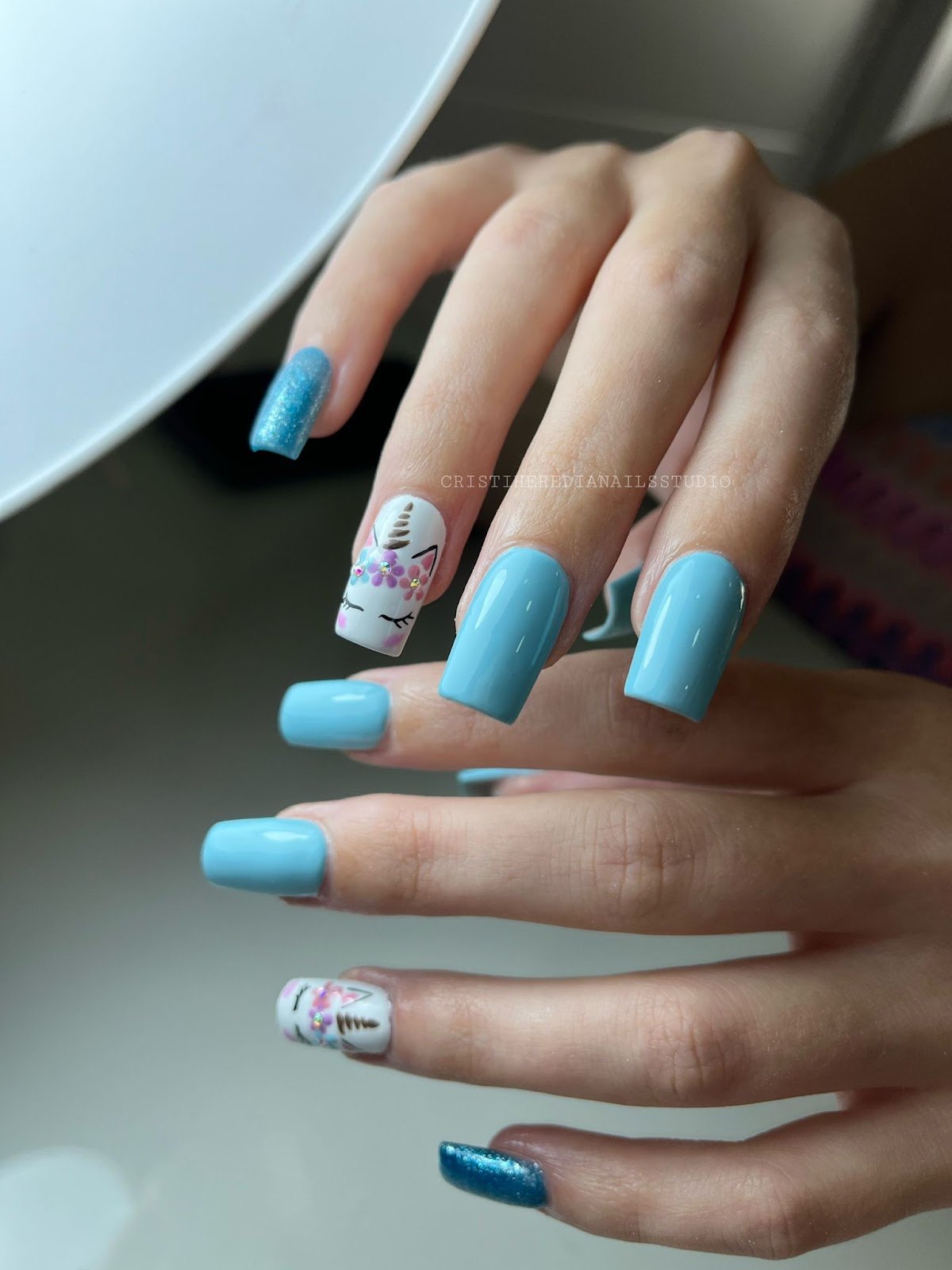 Uñas cuadradas azul celeste con purpurina y un unicornio dibujado a mano